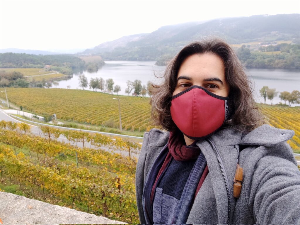 Eu cunha máscara vermella en fronte dun amplo paisaxe de vides e encoro.