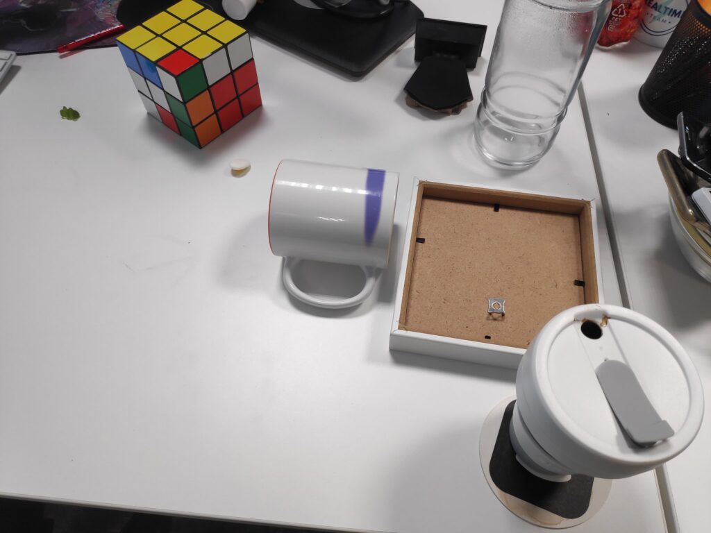Foto de unha mesa con unha caneca deitada, un marco de foto boca abaixo e un cubo de Rubik desordenado.