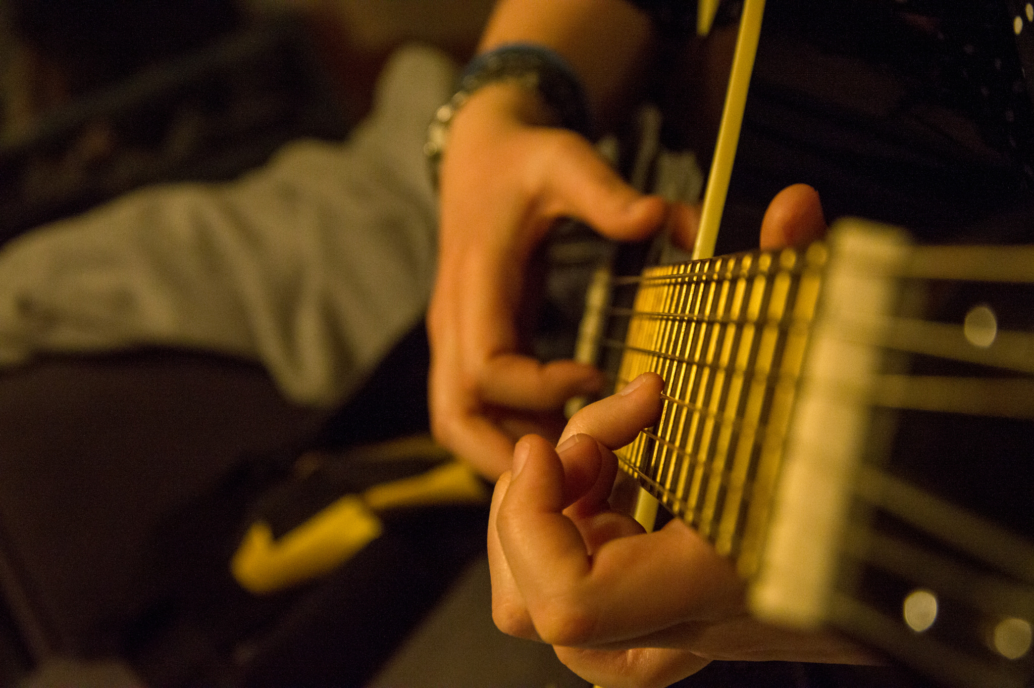 Foto do mástil dunha guitarra tomada desde a punta. As mans dunha rapaza están a tocar.