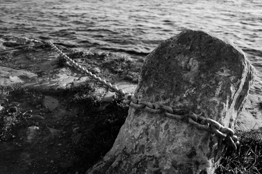 Foto dunha cadea atada a unha pedra que entra no mar.