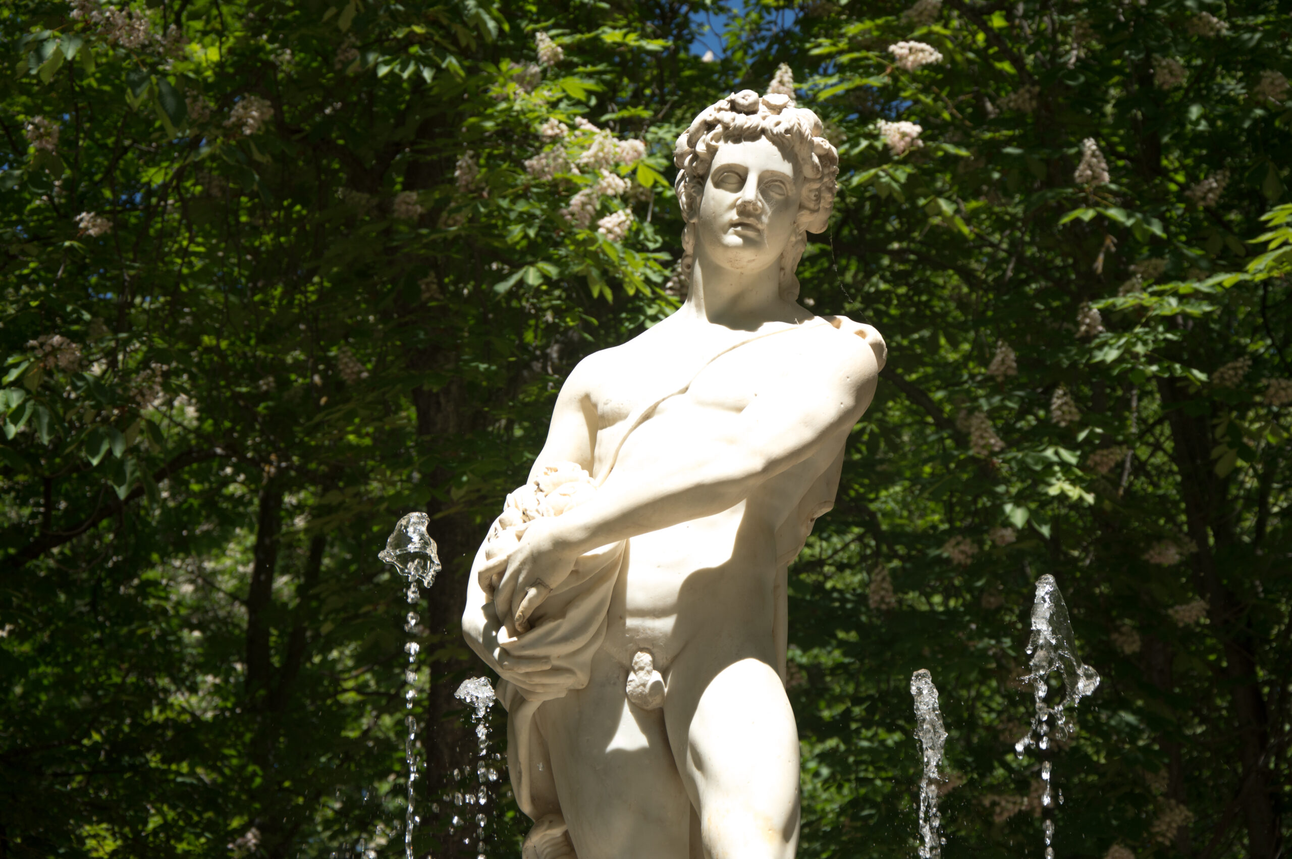 Foto dunha estatua de mármore rodeada de chorros de auga.